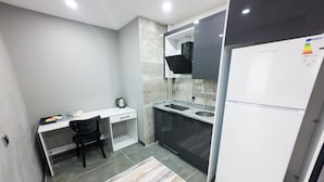 Una cocina compacta con encimera blanca, una silla negra, un refrigerador y un salpicadero de azulejos.