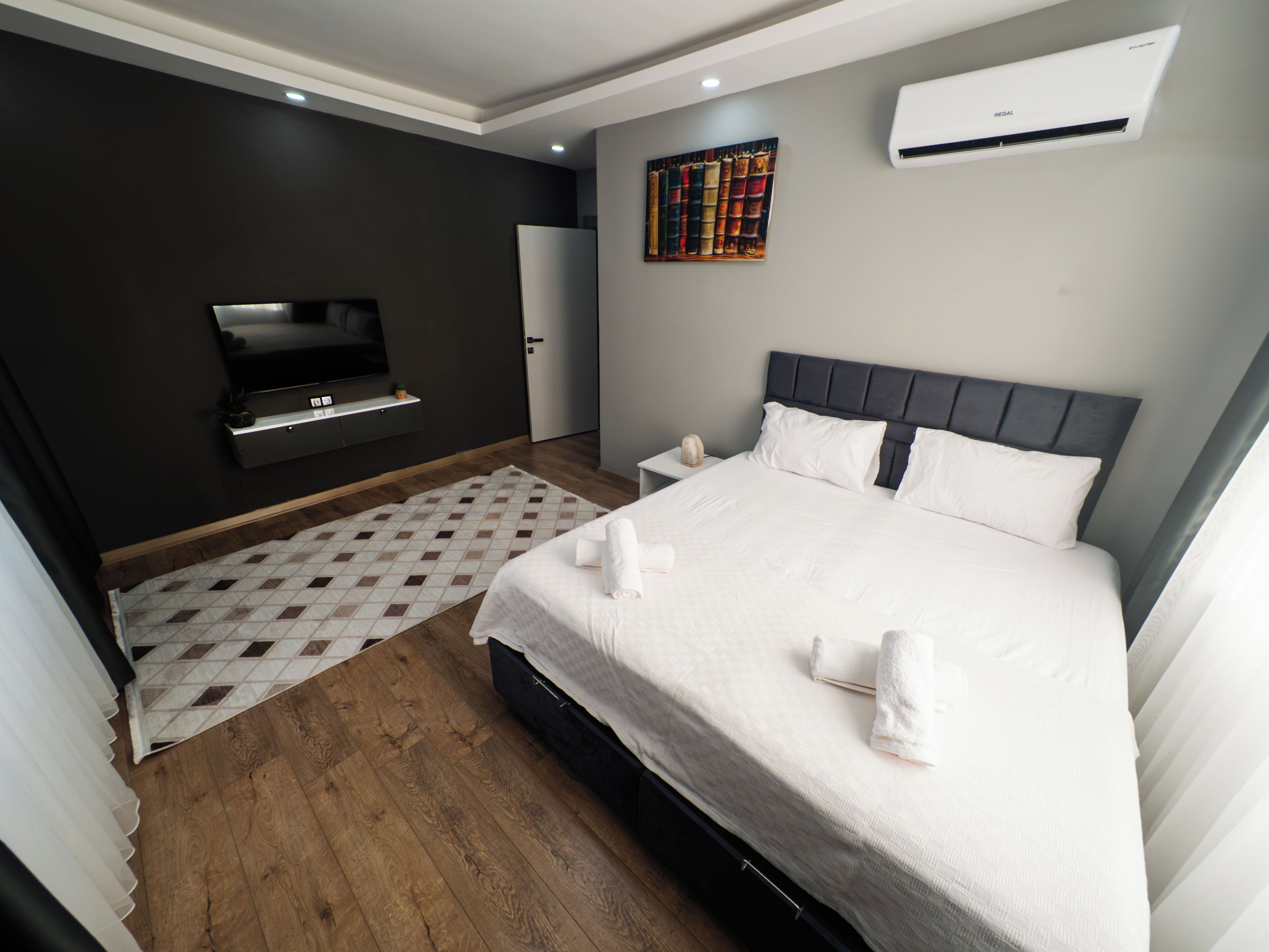 Una habitación de hotel moderna con una cama grande, un televisor de pantalla plana, una estantería y un equipo de aire acondicionado.