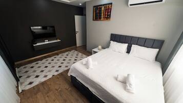 Una habitación de hotel moderna con una cama grande, un televisor de pantalla plana, una estantería y un equipo de aire acondicionado.
