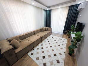 A modern living room with a sectional sofa, a patterned rug, and potted plants.