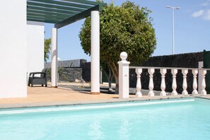 A swimming pool with a white balustrade, a covered seating area, and a stone wall in the background. - 3 Bedroom Villa in Playa Blanca (Yaiza)