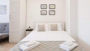 A hotel room with a bed, a nightstand with a plant, and a grey sofa. There are four framed pictures on the wall. - Bogoviceva 1b (Zagreb)