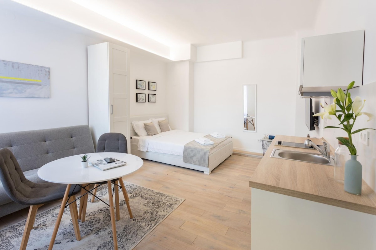 A compact living space with a sofa, a bed, a dining area, and a kitchenette.