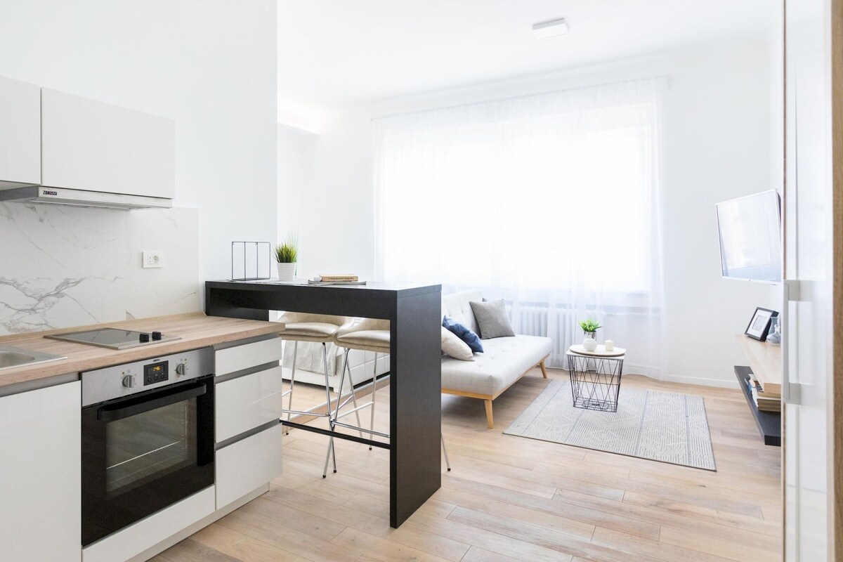 A modern kitchen with a built-in oven and a dining area with a sofa and chairs.