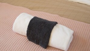 A neatly made bed with a white and black patterned pillow, a blue pillow, and a folded towel on a pink textured bedspread. - G43 (Zagreb)