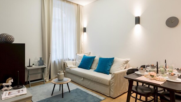 A modern living room with a sofa, a coffee table, a dining table set for two, and a television. - G43 (Zagreb)