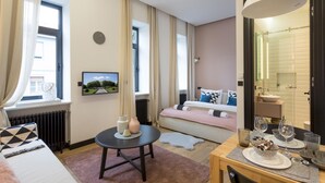 A well-lit hotel room with a bed, bedside table, and a dining area with a table set for two. - G43 (Zagreb)