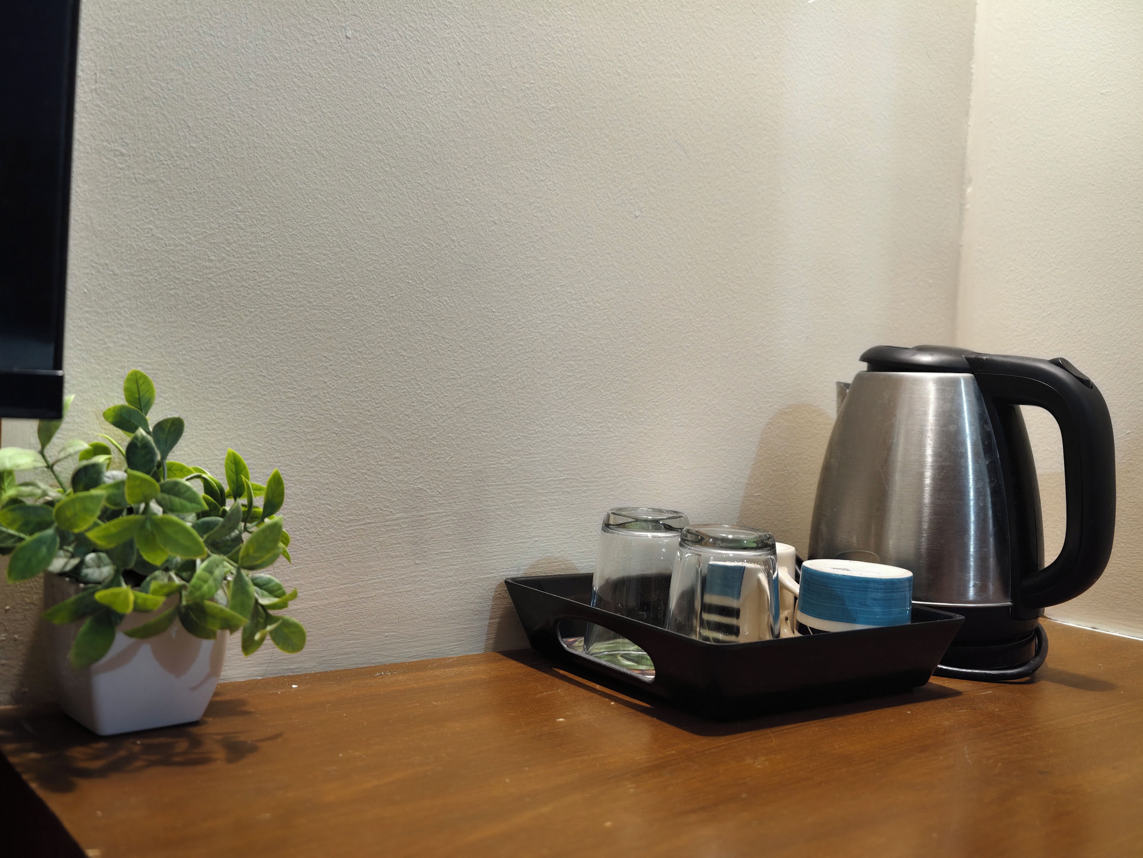 Una mesita con una planta en maceta, una bandeja con hervidor, vasos y una taza.