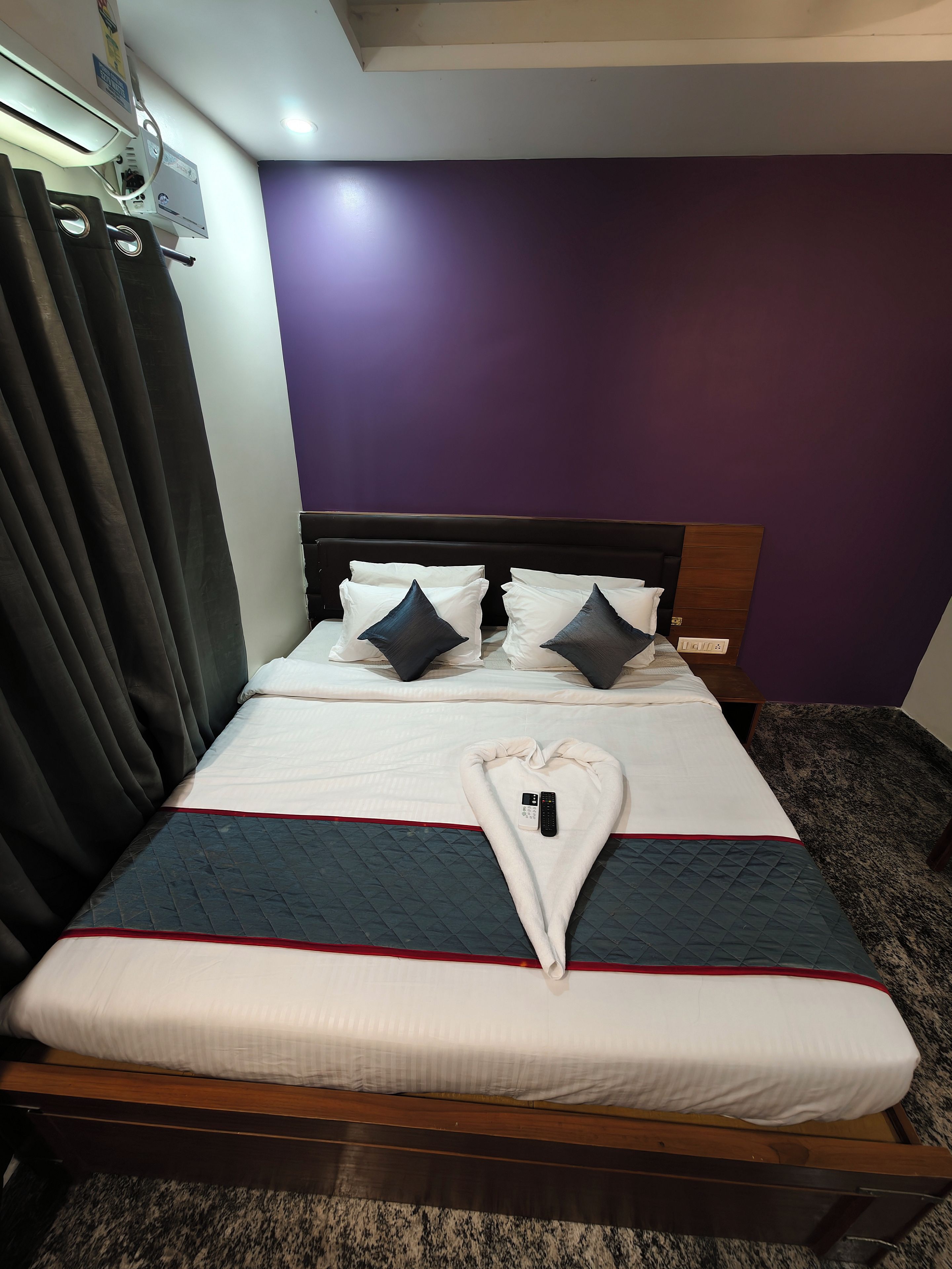 Una habitación de hotel con una cama, una toalla con forma de corazón y un control remoto sobre la cama.