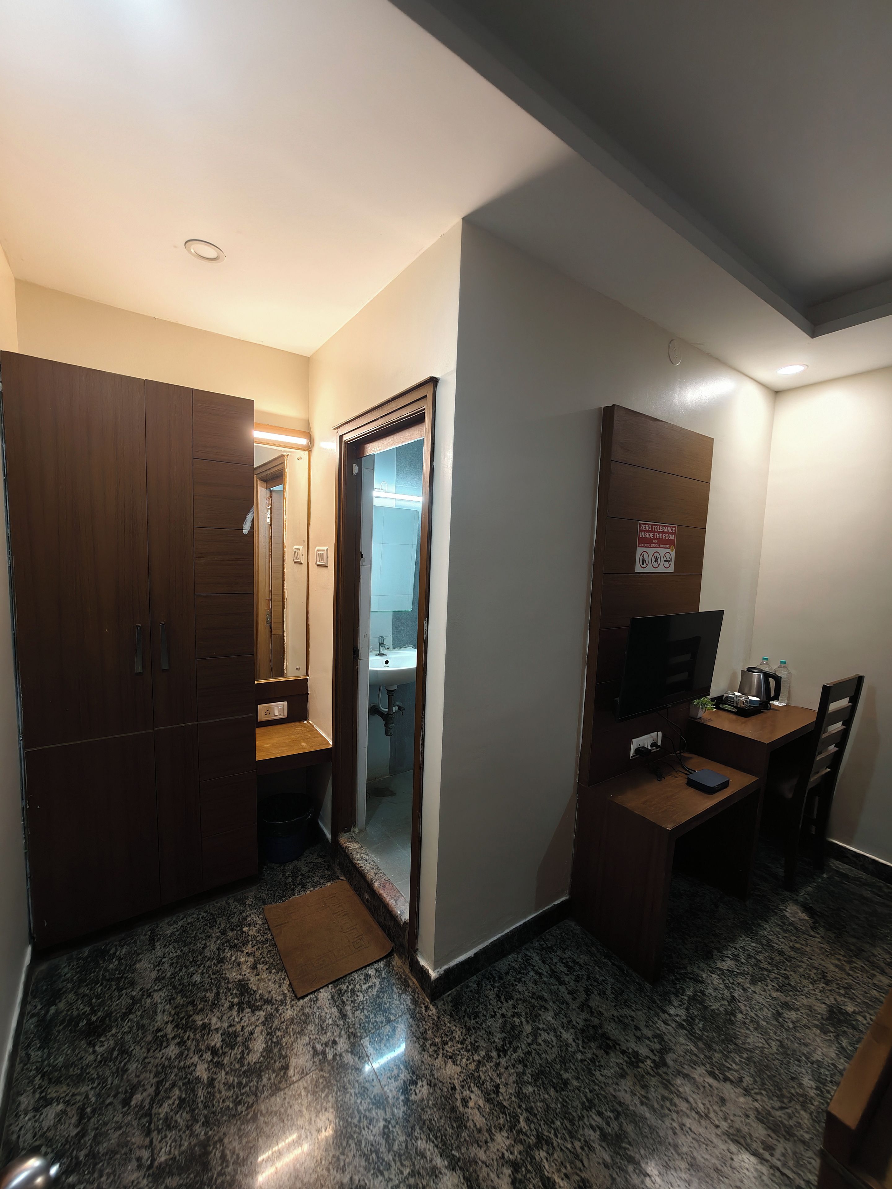 A compact room with a wardrobe, a desk with a television, a sink, and a mirror.