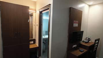 A compact room with a wardrobe, a desk with a television, a sink, and a mirror.