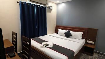 Een hotelkamer met een bed, een bureau, een stoel, een airconditioning en een plafondventilator.