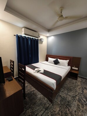 A hotel room with a bed, a desk, a chair, an air conditioning unit, and a ceiling fan.