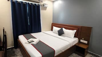 Et hotelværelse med en seng, et natbord, en aircondition og en ventilator.