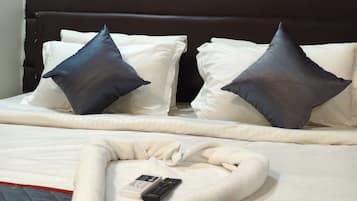 A neatly made bed with white and dark pillows, a remote control, and a folded blanket on a bed with a red trim.