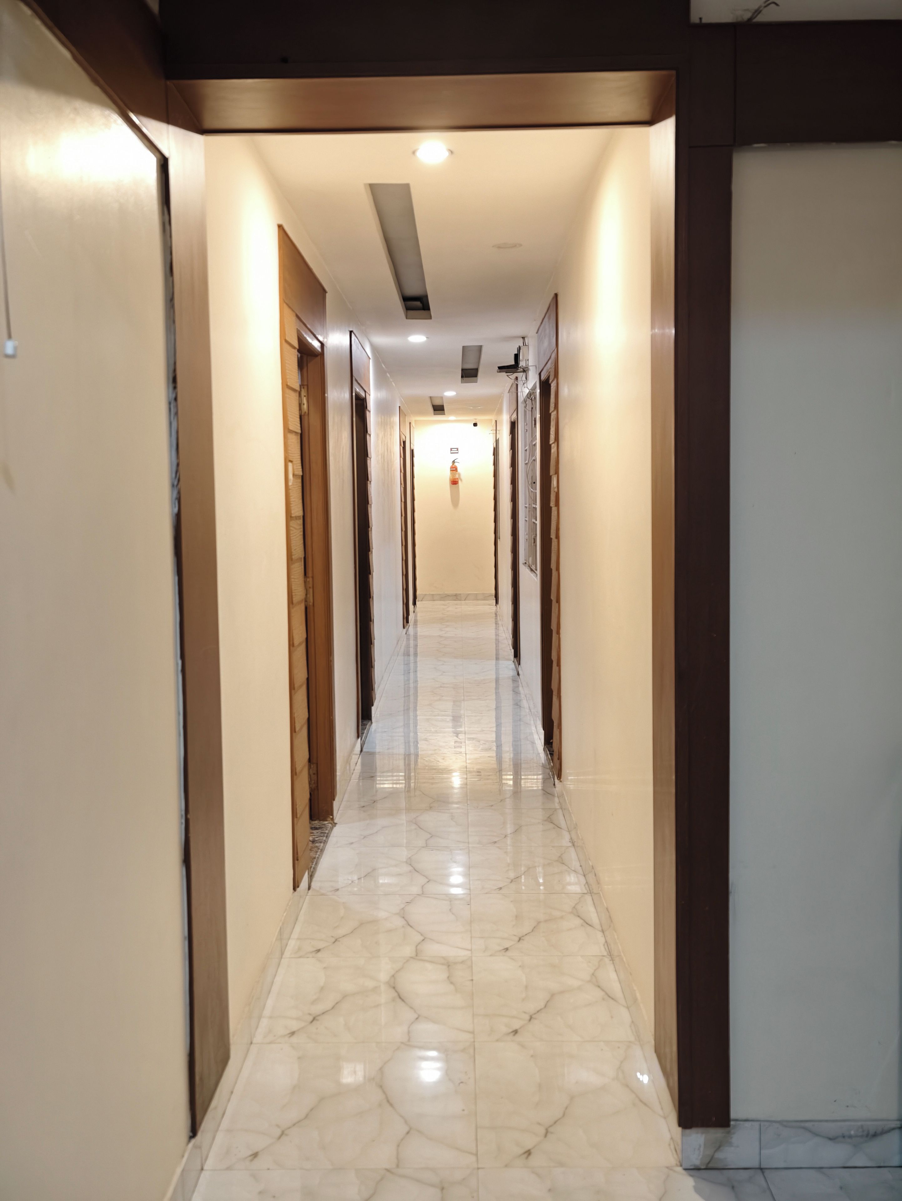 A corridor with a polished marble floor, wooden doors, and recessed lighting.