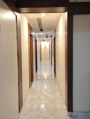 A corridor with a polished marble floor, wooden doors, and recessed lighting.