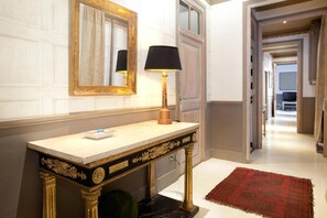 A hallway with a marble console table, a gold-framed mirror, and a red rug. - Hohomes - Centric Entire Barcelonian Flat (Barcelona)