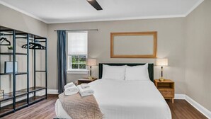 A neatly made bed with a green headboard, two bedside tables with lamps, a window with curtains, and a wall-mounted mirror. - Cottontown Cottage | Fenced Yard & Covered Patio (Columbia)