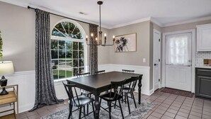 A dining area with a table and chairs, a window with curtains, a chandelier, and a kitchen area with cabinets. - Cottontown Cottage | Fenced Yard & Covered Patio (Columbia)