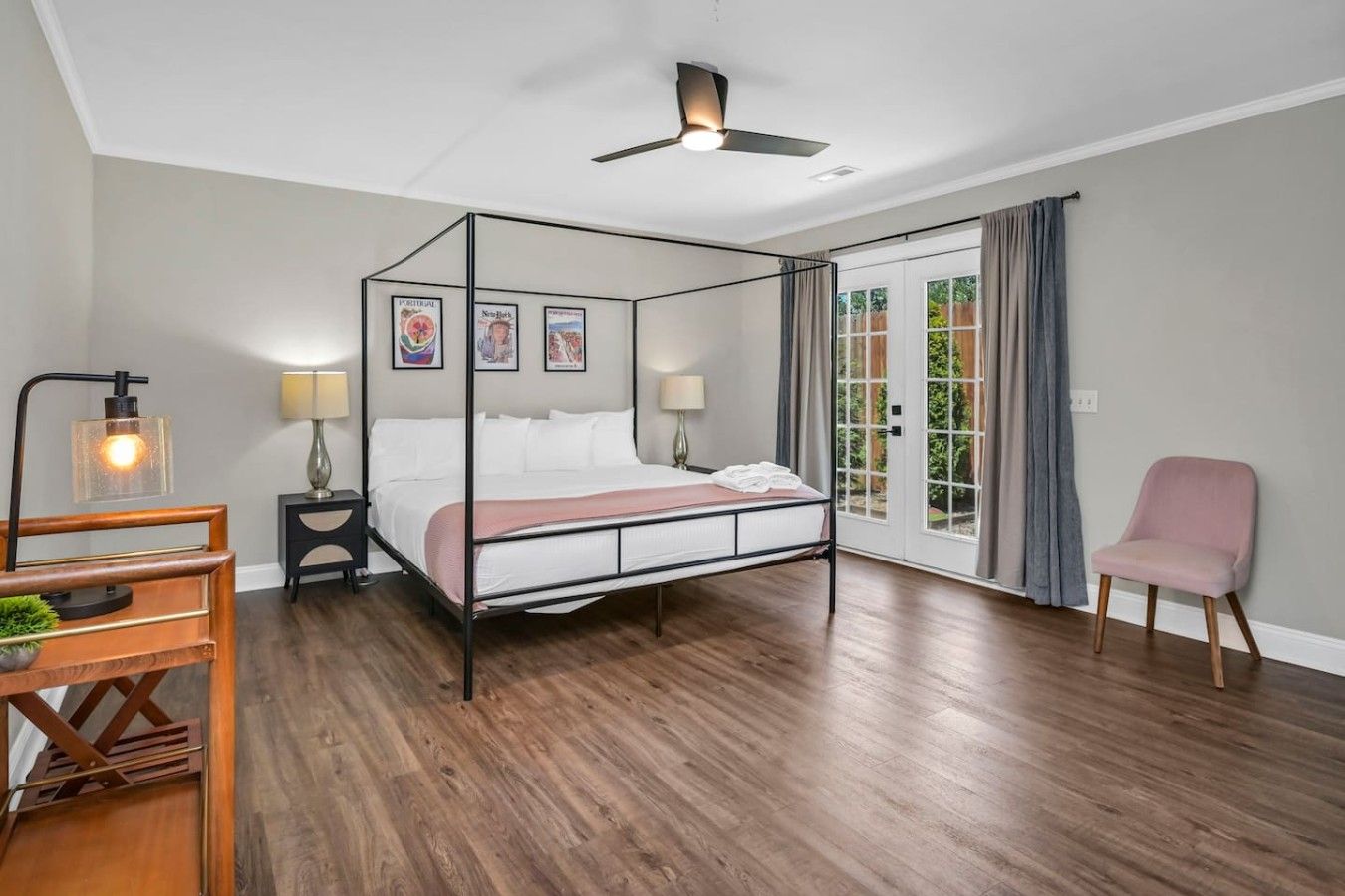 A four-poster bed with a canopy, bedside tables with lamps, a chair, and a view through a glass door to the outside.