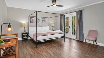 A four-poster bed with a canopy, bedside tables with lamps, a chair, and a view through a glass door to the outside.