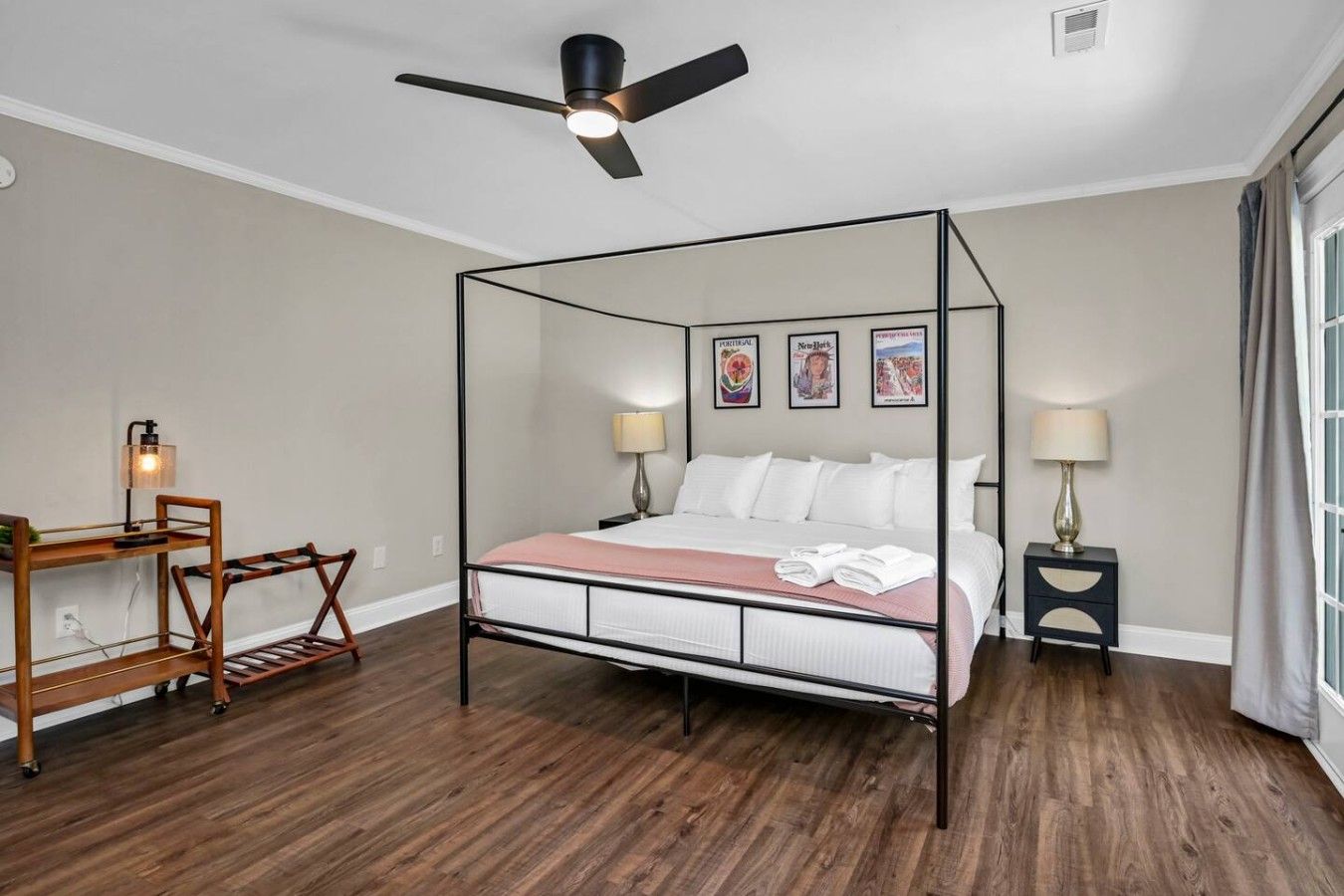 A four-poster bed with a wooden frame, a desk with a lamp, and a nightstand with a lamp.