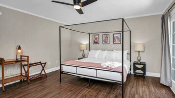 A four-poster bed with a wooden frame, a desk with a lamp, and a nightstand with a lamp.