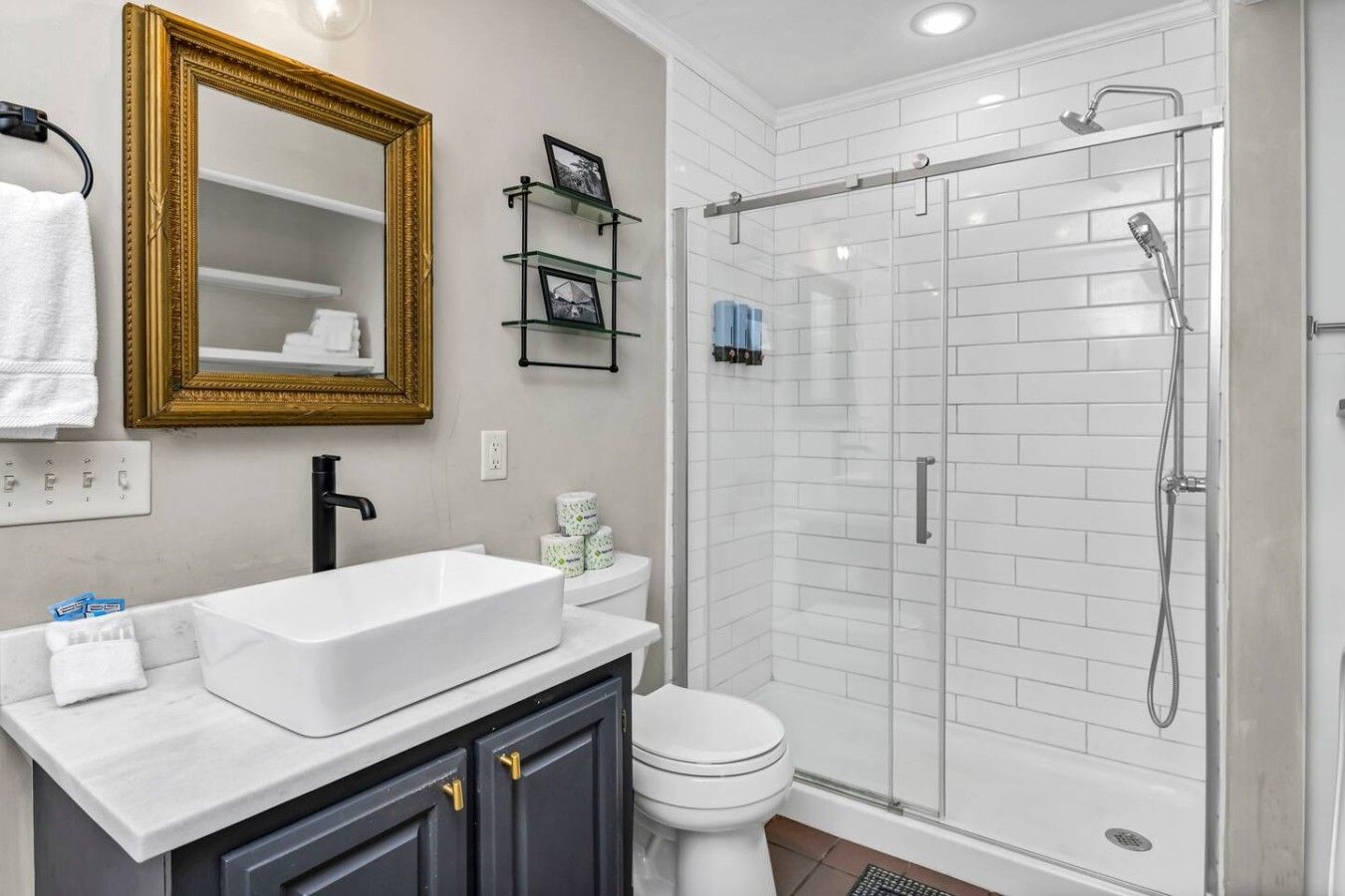 A bathroom with a white sink, a toilet, a glass shower enclosure, and a gold-framed mirror.