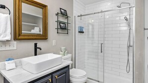 A bathroom with a white sink, a toilet, a glass shower enclosure, and a gold-framed mirror. - Cottontown Cottage | Fenced Yard & Covered Patio (Columbia)