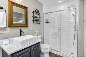Une salle de bain avec un lavabo blanc, des toilettes, une douche en verre et un miroir avec un cadre doré.