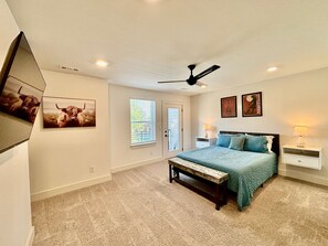Een slaapkamer met een bed, een bankje, een plafondventilator, een raam en wanddecoratie.