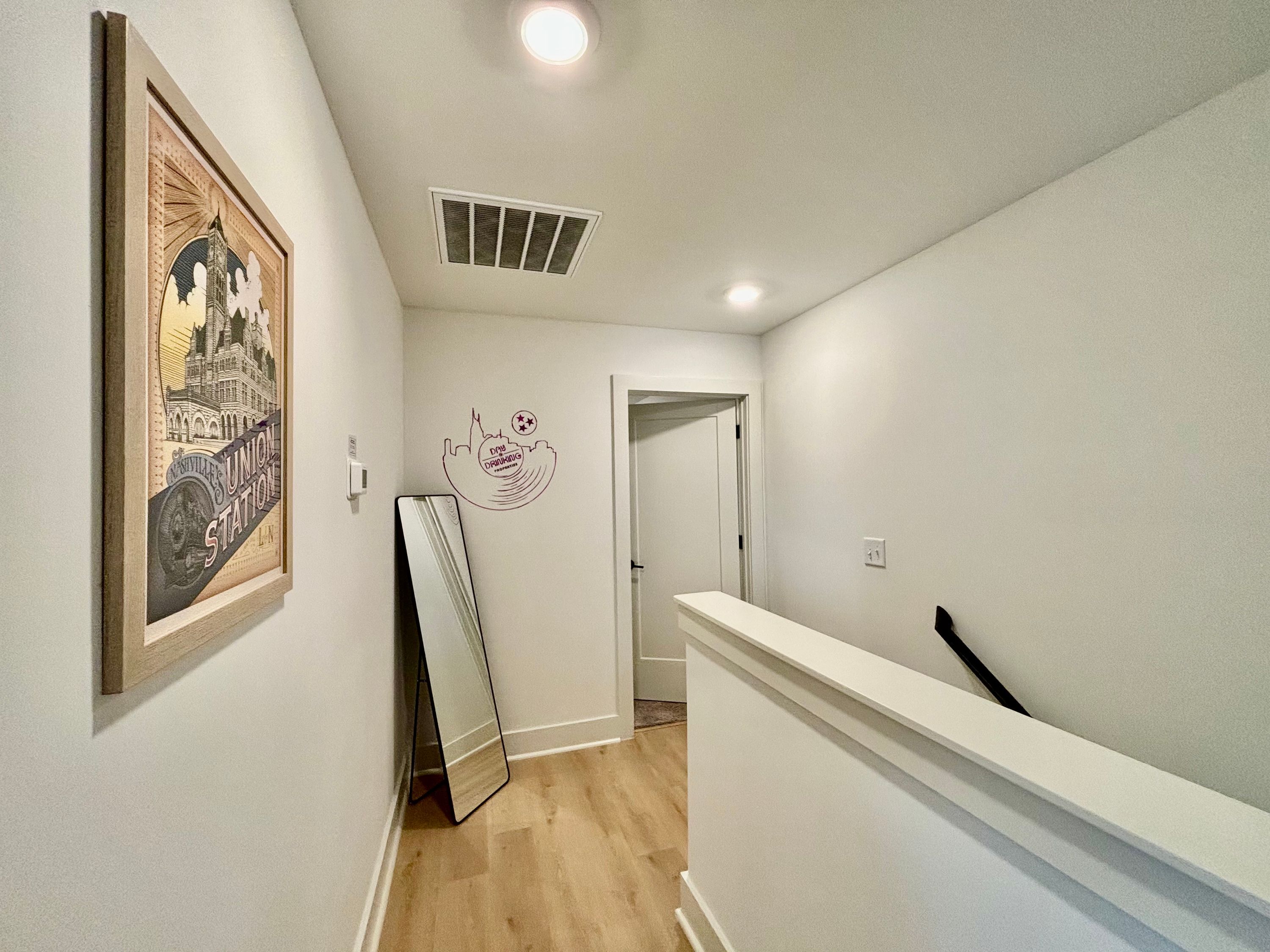 Ein Flur mit einem gerahmten Bild einer Bahnhaltestelle, einem an der Wand angelehnten Spiegel und einer Tür, die in einen anderen Raum führt.