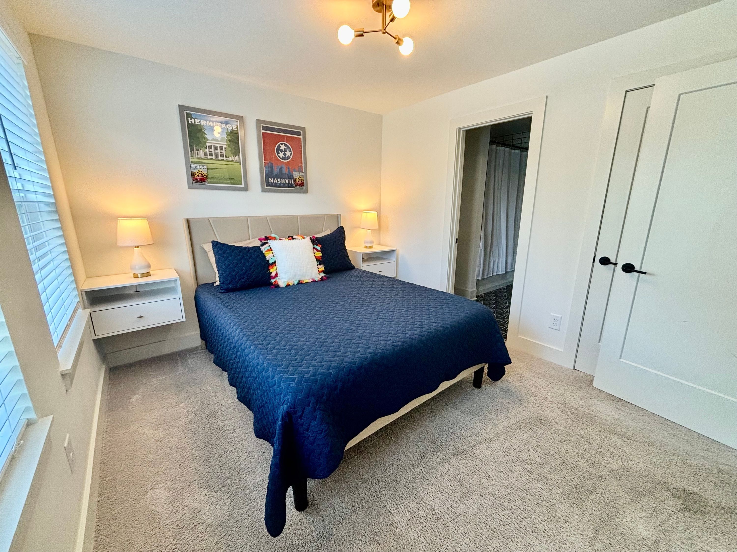 A bedroom with a bed, two nightstands, a lamp, a door, and two posters on the wall.