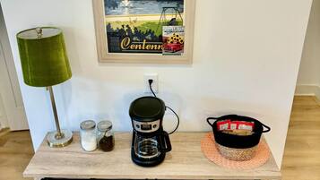A wooden coffee station with a coffee maker, jars, and a basket.