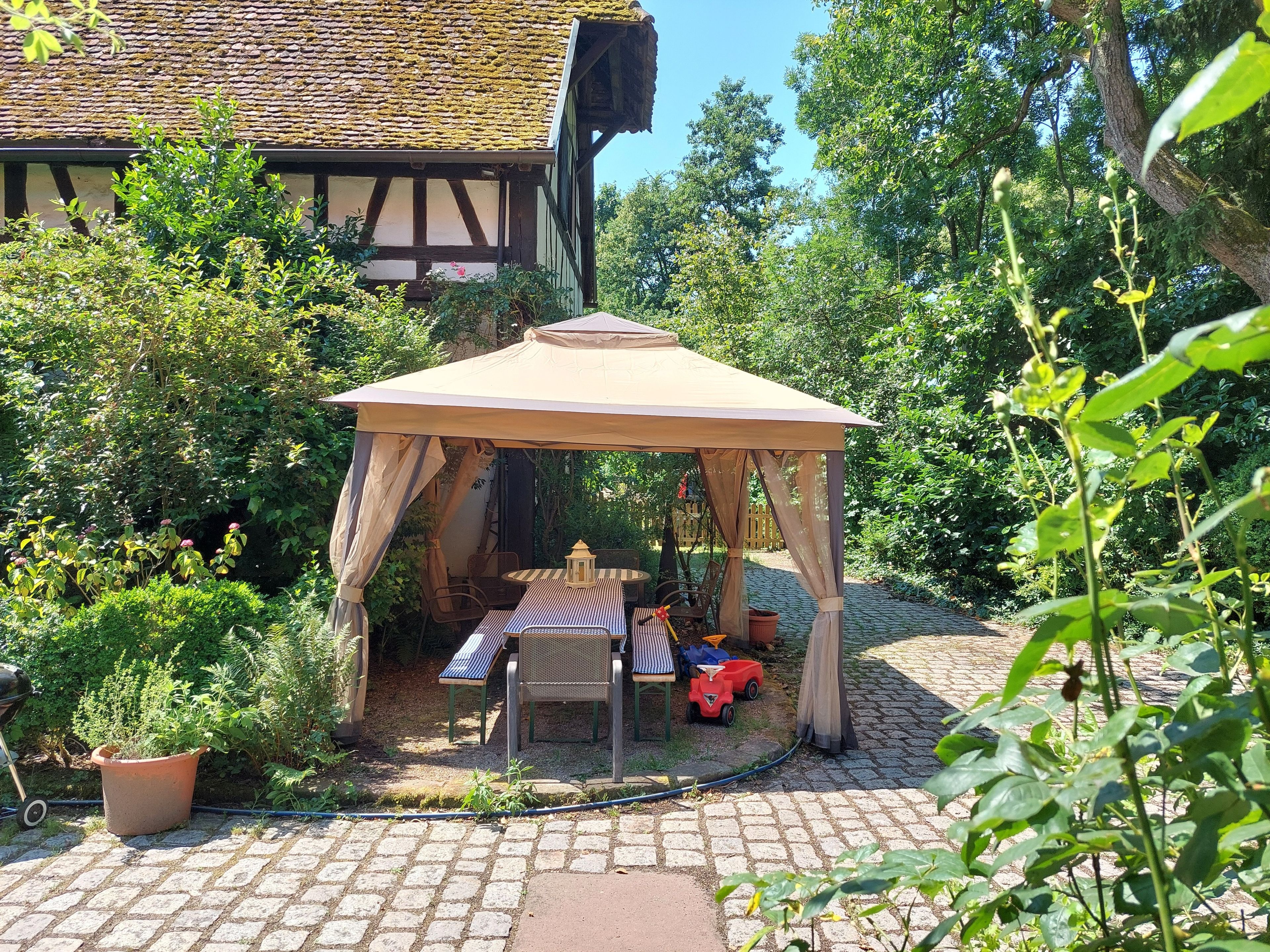 Un jardin agrémenté d’un kiosque, d’une table, de chaises et d’une plante en pot.