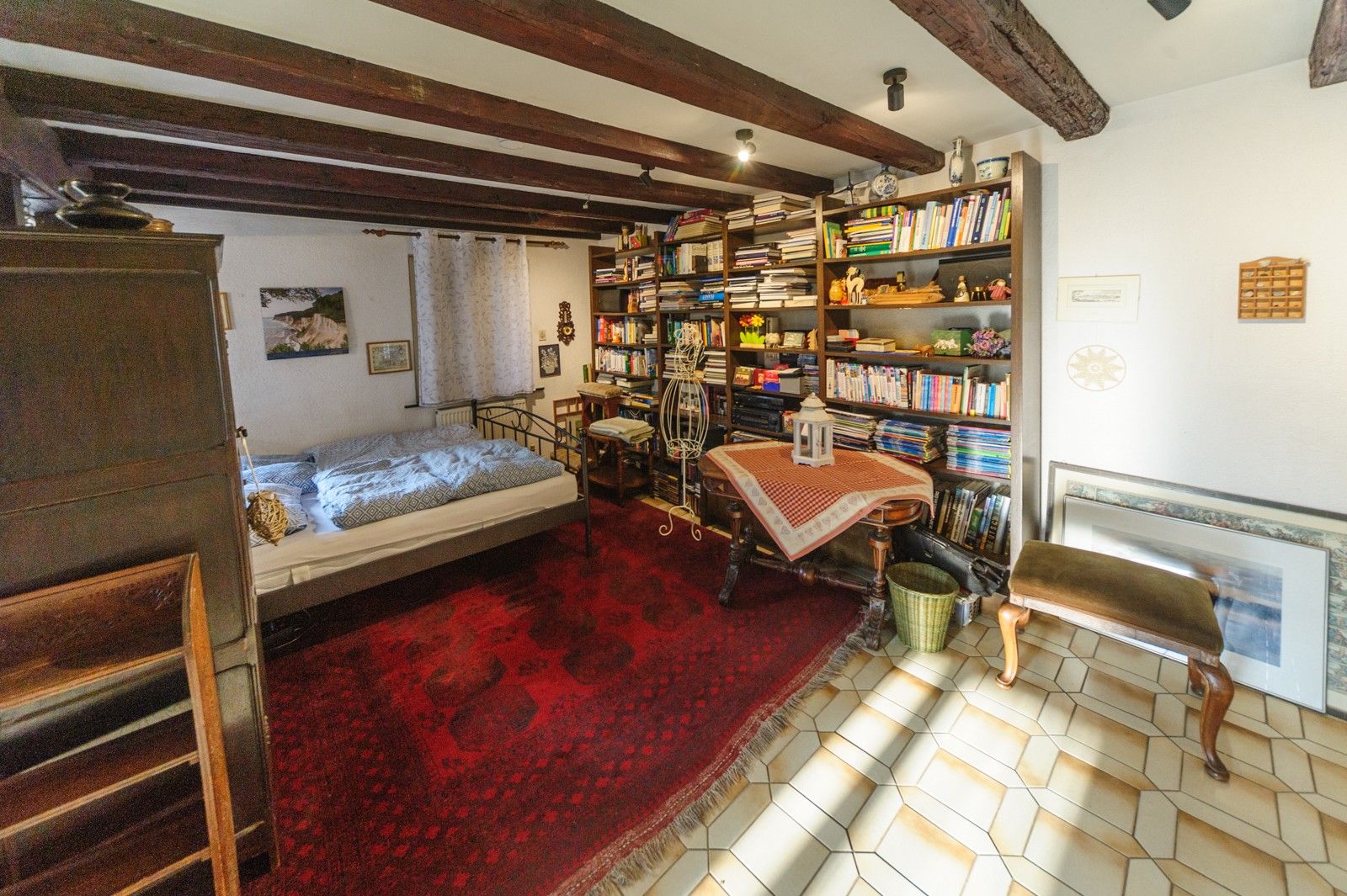 Une pièce comprenant un lit, une bibliothèque, une petite table avec une lanterne et une chaise.