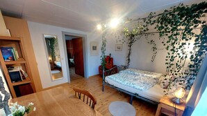 Een kamer met een bed, een houten tafel, een stoel, een boekenkast en een deuropening naar een andere kamer.