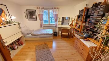 A cozy bedroom with a bed, a desk, a bookshelf, and a radiator.