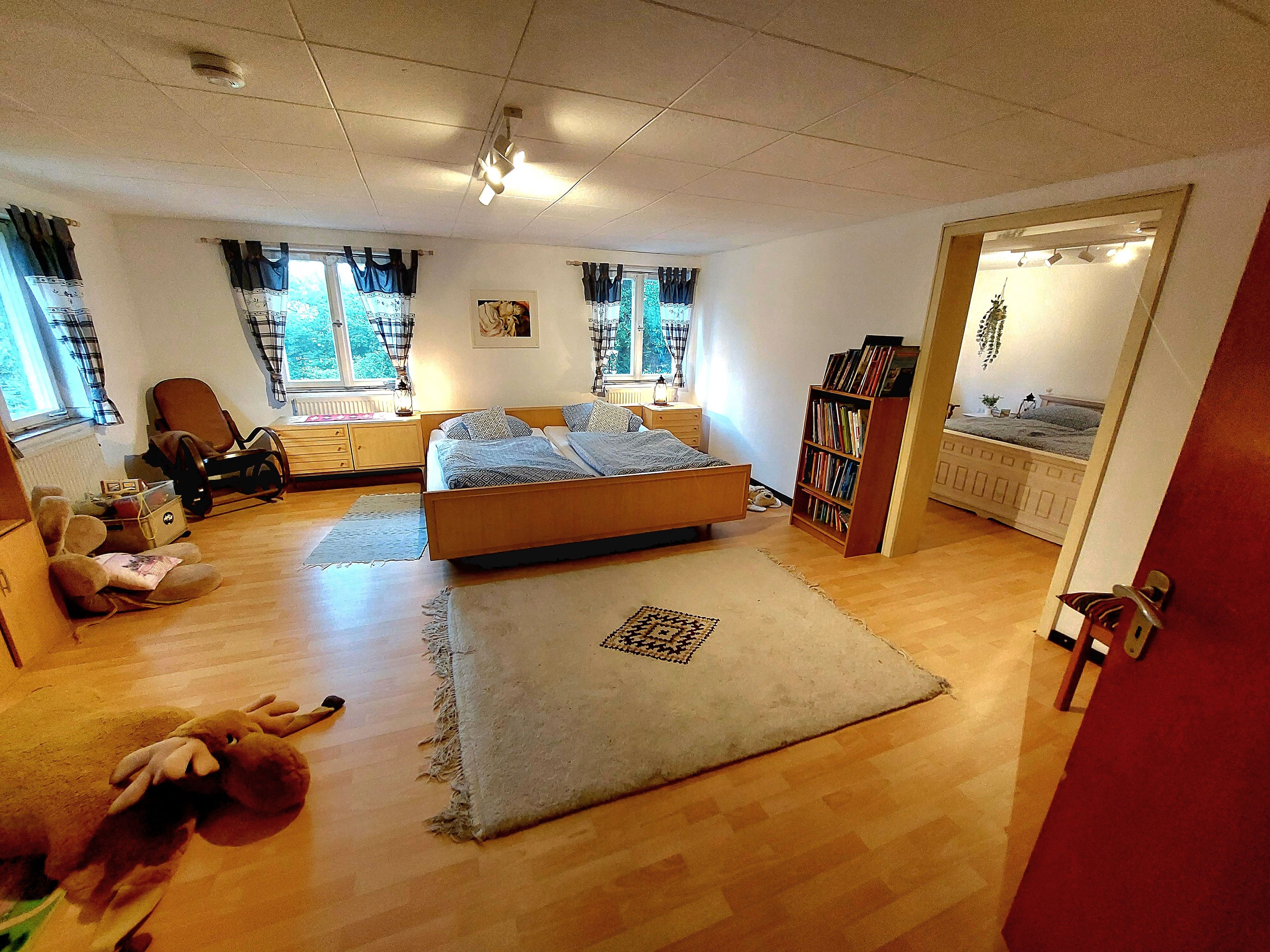 Een slaapkamer met een bed, een boekenkast, een stoel, een raam met gordijnen en een deur.