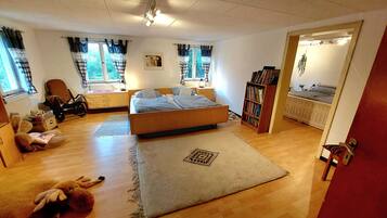 Een slaapkamer met een bed, een boekenkast, een stoel, een raam met gordijnen en een deur.