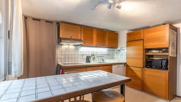A compact kitchen with wooden cabinets, a tiled backsplash, a built-in microwave, and a dining table with stools.