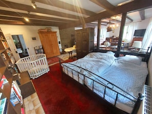 A bedroom with a large bed, a crib, a wooden wardrobe, and a bookshelf.