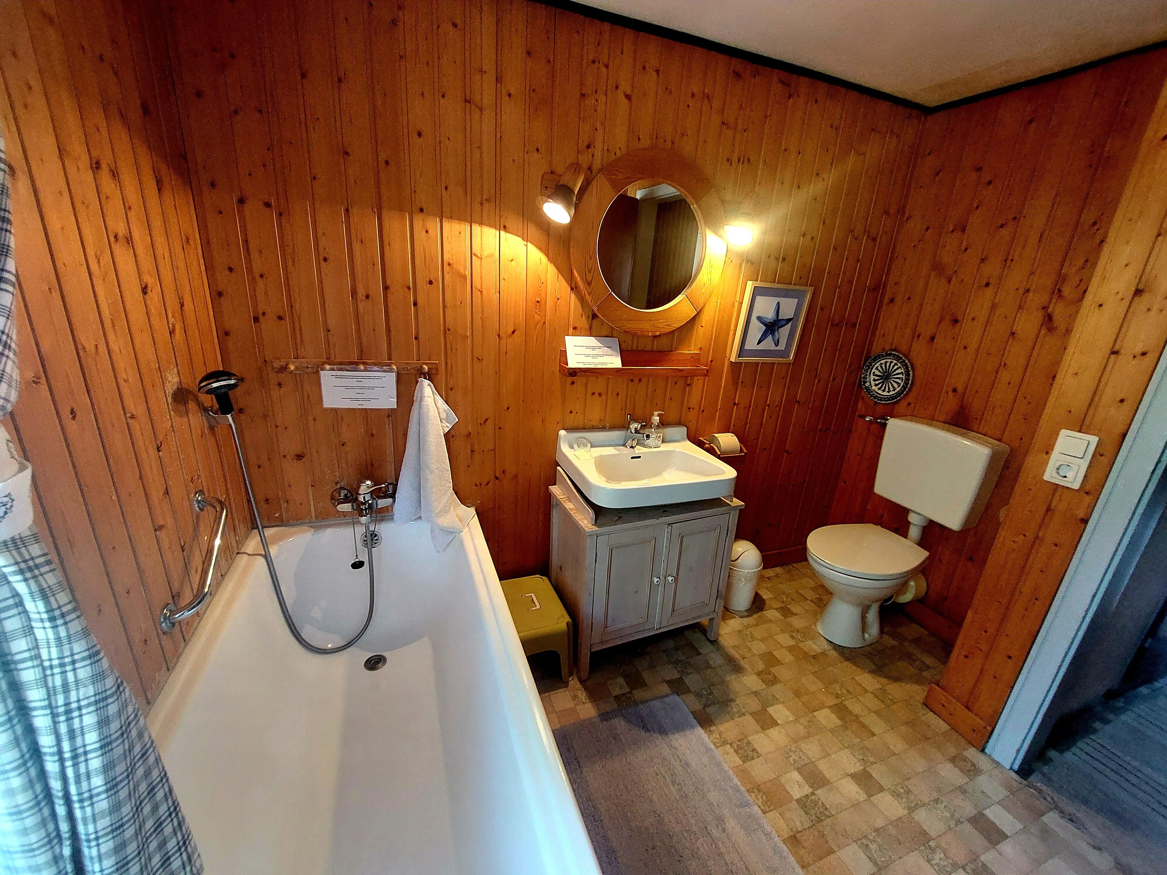 Ein Badezimmer mit Holzvertäfelung, einer Badewanne, einem Waschbecken, einer Toilette und einem Spiegel.