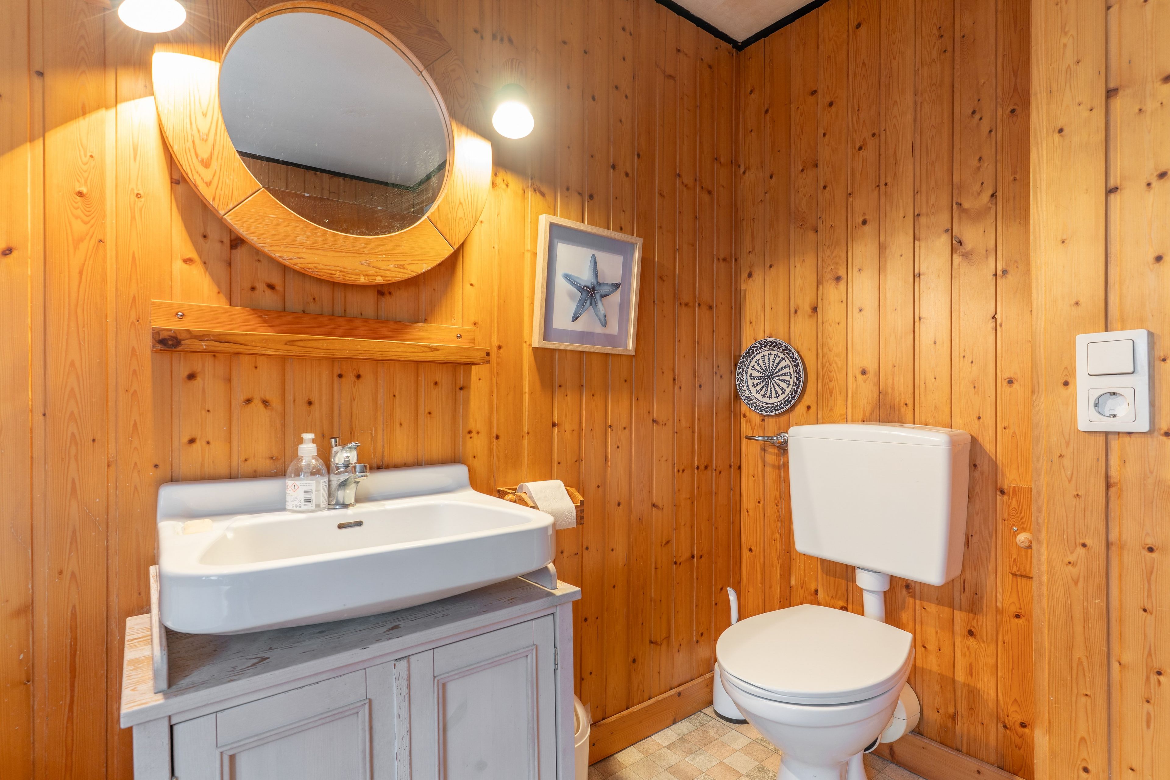 Une salle de bain aux murs lambrissés, avec un lavabo blanc, des toilettes et un miroir.