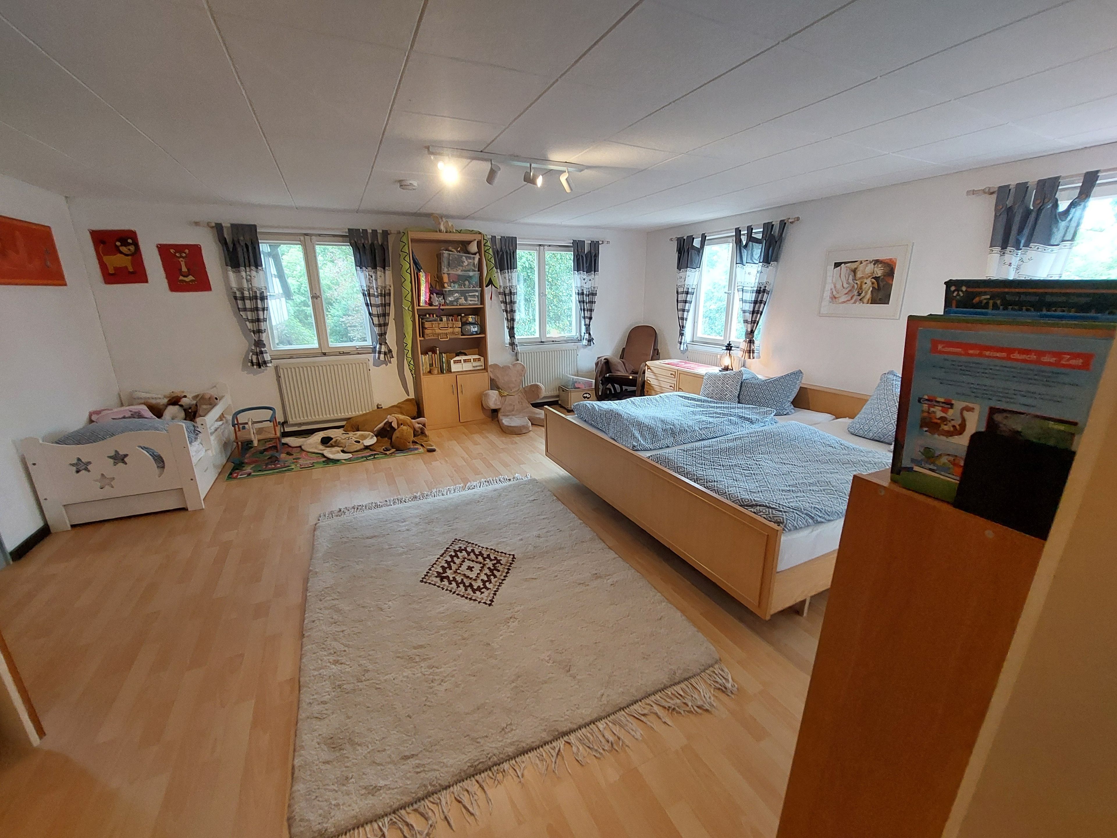 Ein Schlafzimmer mit einem Bett, einem Schreibtisch, einem Stuhl, einem Heizkörper und einem Fenster mit Vorhängen.