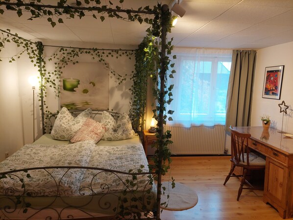 A bedroom with a bed, a desk, and a chair. There is ivy hanging from the ceiling and walls.
