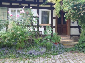 A traditional half-timbered house with a wooden door, a bench, and a garden with flowers and plants.
