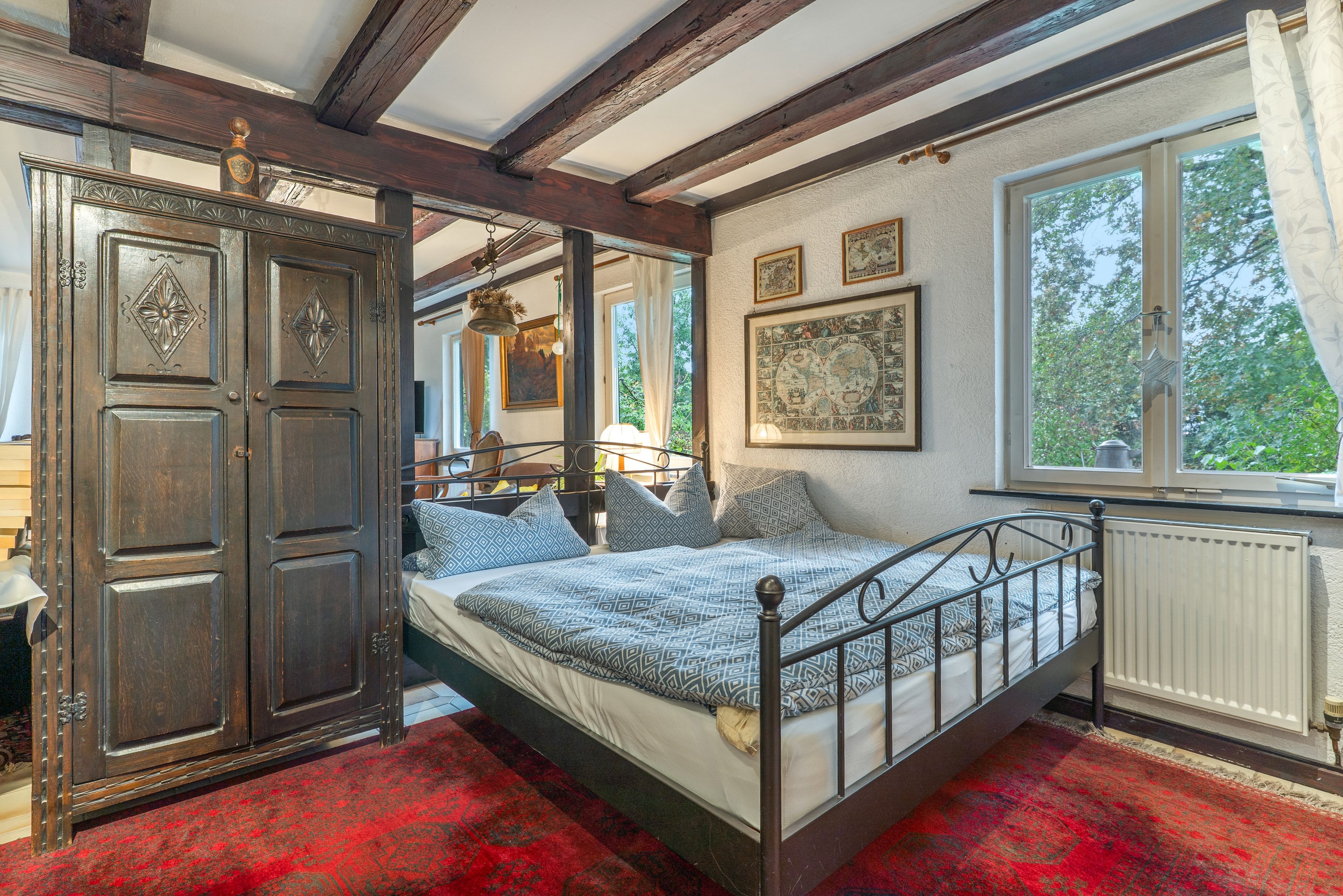 Une chambre traditionnelle avec un lit à baldaquin, une grande armoire en bois et une fenêtre donnant sur la forêt.