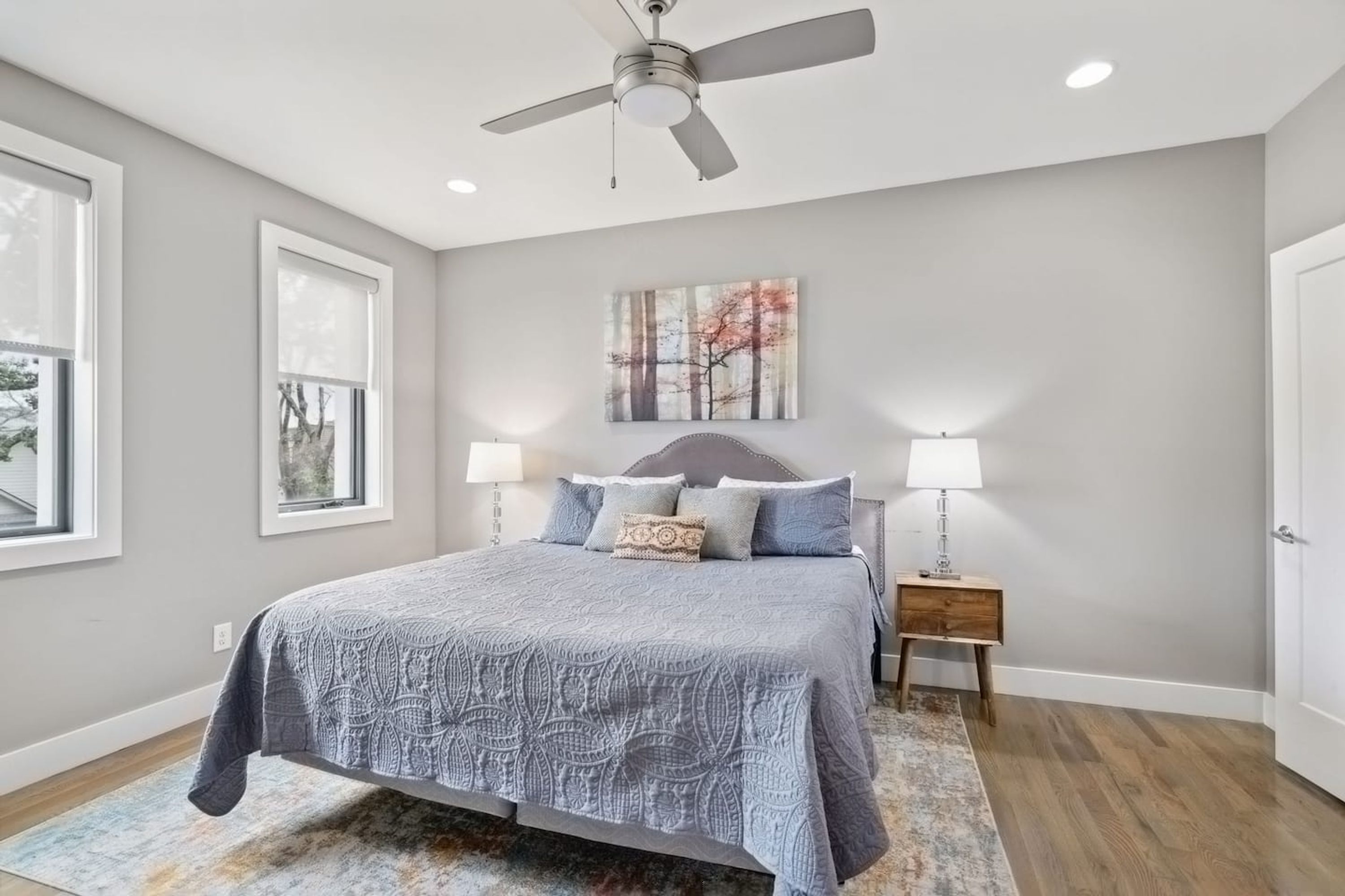 A bedroom with a bed, two bedside tables, a ceiling fan, a window, and a painting on the wall.
